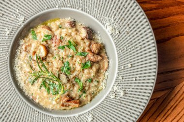 Taze bitkilerle süslenmiş kremalı mantarlı risotto ve parmesan peyniri ahşap bir masanın üstünde geniş çerçeveli bir seramik kasede servis edilir. Boşluğu kopyala.