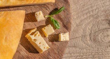 Kırsal ahşap bir tahta üzerinde taze otlar ve hafif ahşap arka planda küp İsviçre peyniri. Boşluğu kopyala, üst görünüm