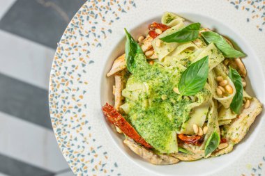 Pesto soslu Tagliatelle makarnası, güneşte kurutulmuş domates, çam fıstığı ve seramik tabakta fesleğen. Üst Manzara. metin için boşluk kopyala,