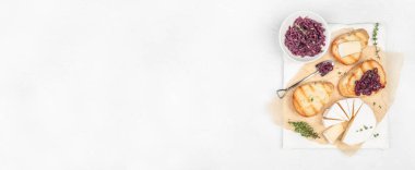 Dilimlenmiş peynir çarkı, bir kasede karamelize edilmiş kırmızı soğan, ve malzemelerle birlikte kızarmış ekmek dilimleri, parşömen kağıdında taze kekik ile servis edilen beyaz mermer tahta, üst manzara. Boşluğu kopyala.