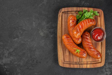 Izgara sosis, maydanozlu ve ketçaplı, ahşap tahtada servis edilen koyu arka planda. Üst Manzara. Boşluğu kopyala