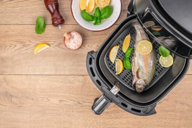 Limon dilimleri ve fesleğenli tam balık ahşap masada tavada pişiyor. Üst Manzara. Boşluğu kopyala.