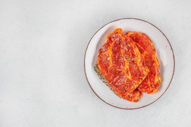 Baharatlı ve beyaz tabakta bitkilerle marine edilmiş domuz bifteği. Üst Manzara. Boşluğu kopyala.