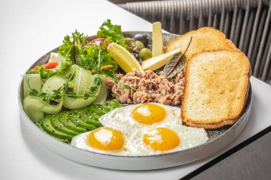 Kahvaltı tabağı, kızarmış yumurta, ton balığı, avokado tostu peynir ve taze sebze..