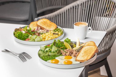 Sağlıklı kahvaltı tabakları, yumurtalı tost, sebze ve beyaz bir masada kahve..