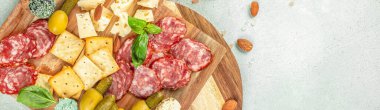 Top view of antipasto platter with salami, cheese, olives, crackers, and herbs on wooden board with copy space for text.