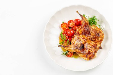 Healthy grilled quail served with fresh cherry tomatoes and herbs, nutritious gourmet poultry dish on white plate. top view. copy space.