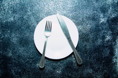 Karanlık bir arkaplanda boş tabak ve çatal