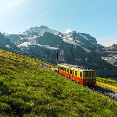 Küçük elektrikli kırmızı turist treni olan çarklı demiryolu. Jungfraujoch, Kleine Scheidegg, Grindelwald, Bernese Oberland, İsviçre, Avrupa 'daki Karlı Jungfrau Dağları ve kırmızı yolcu treni