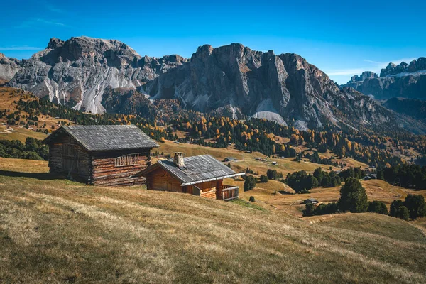 山の牧草地のかわいい小さなログハウスとバックグラウンドの美しい山の尾根 プエズオドル山グループ ドロマイト イタリア ヨーロッパ ロイヤリティフリーのストック画像