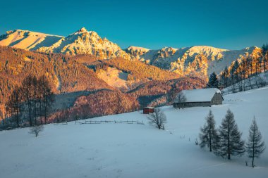 Güneşin batışında arka planda, karla kaplı ahşap kulübe ve görkemli yüksek dağlar, Bucegi dağları, Karpatlar, Romanya, Avrupa