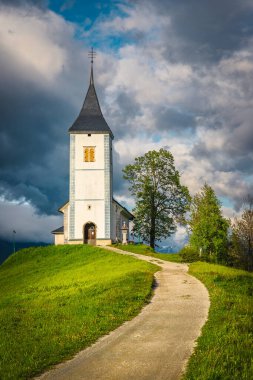 Tepedeki bahar manzarası ve dağ kilisesi. Kırsal çakıl yolu ve arka planda Aziz Primoz kilisesi olan harika bir yer, Jamnik köyü, Slovenya, Avrupa