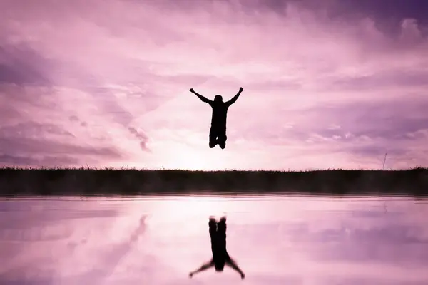 夕日を背景に池の上を飛び越える男 ロイヤリティフリーのストック画像