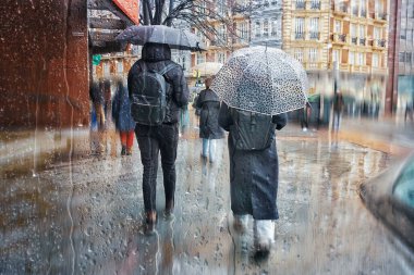 Kışın yağmurlu günlerde elinde şemsiyeyle sokakta yürüyen yayalar. 
