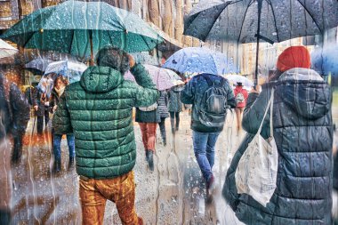 Kışın yağmurlu günlerde elinde şemsiyeyle sokakta yürüyen yayalar. 
