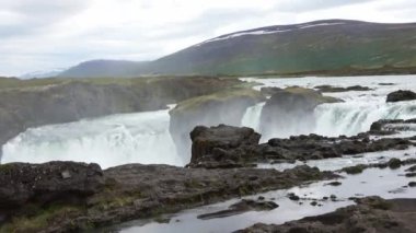 Muhteşem Godafoss şelalesi İzlanda manzarasında kayalar ve otlarla