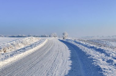 Kışın güneşli ve mavi gökyüzü olan karla kaplı bir kır yolu manzarası