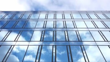 Bir ofis binasının cam cephesinden yansıyan bulutlarla dolu mavi bir gökyüzünün zaman akışı..