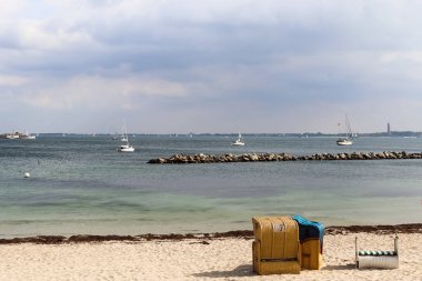 Many sailboats on a sandy beach in Germany with some beach chairs clipart