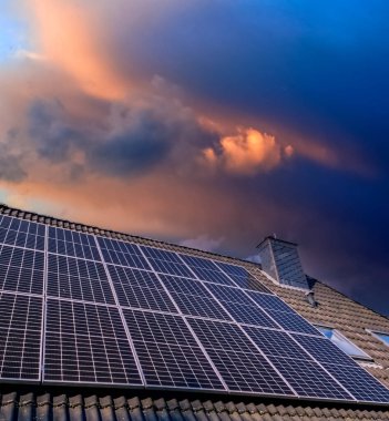 Güneş panelleri güneş batarken bir evin çatısında temiz enerji üretiyor.