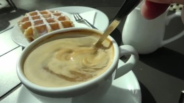 Gözlemelerle dolu bir masada bir fincan kahveye süt karıştırmak..