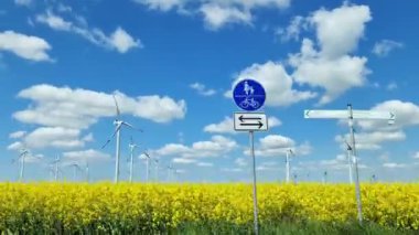 Almanya 'da temiz enerji üreten büyük bir yel değirmeni parkı boyunca giden bir arabanın yan görüntüsü.