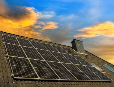 Güneş panelleri güneş batarken bir evin çatısında temiz enerji üretiyor.