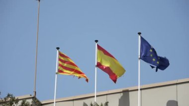 Mavi gökyüzüne karşı rüzgarda dalgalanan bir Katalan bayrağı.