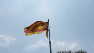 Mavi gökyüzüne karşı rüzgarda dalgalanan bir Katalan bayrağı.