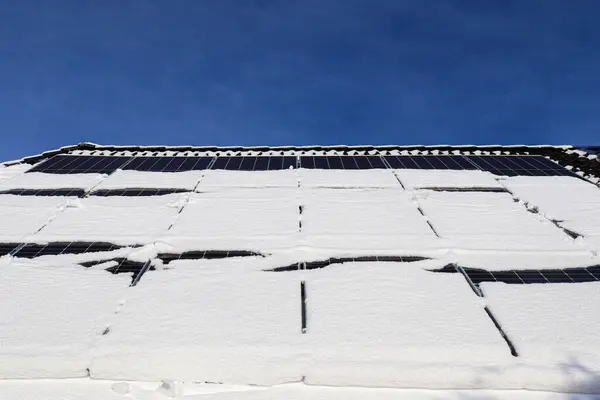 Solar panels covered in snow during wintertime for clean energy on a roof of a residential house