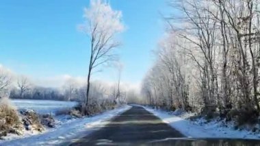 Hareket halindeki bir arabanın ön camından karla kaplı bir köy yoluna bak..