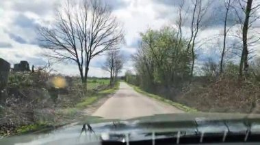 Hareket halindeki bir arabanın ön camından yan tarafında ağaçlar ve çalılar olan küçük ve dar bir köy yoluna bak..