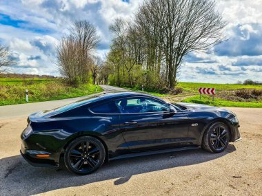 Kiel, Almanya - 04. Mayıs 2024: Güneşli bir havada bir kır yolunda park edilmiş siyah bir Ford Mustang modeli