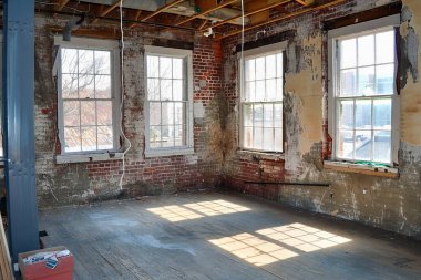 Kısmen yenilenmiş tuğla duvarları, yeni pencereleri ve yarı boyanmış duvarları olan bir oda.