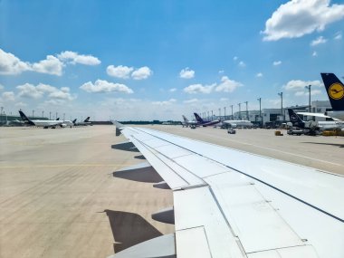 Münih, Almanya - 22 Haziran 2024: Münih Havaalanı 'ndaki diğer park halindeki uçaklara bir yolcu uçağının kanadı üzerinden bakın