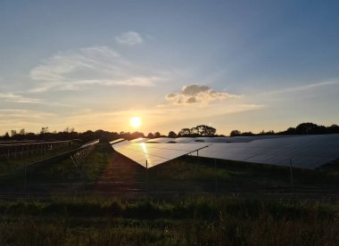 Güneş modüllerine yansıyan gün batımının ışığıyla enerji üretimi için bir güneş parkının karanlık silueti.