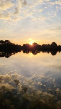 Koyu turuncu renkte rüya gibi bir gün batımı gölün suyuna yansıyor.