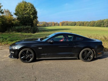 Kiel, Almanya - 05. Aralık 2024: Siyah bir 2018 Ford Mustang modeli bir kır yolunun kenarına park edildi