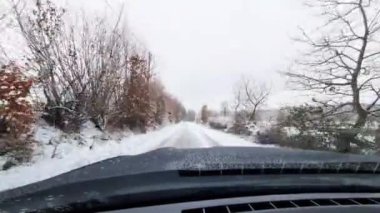 Almanya 'nın ağaçlık bir bölgesinde, karla kaplı bir köy yolunda hareket halindeki bir arabanın görüntüsü.