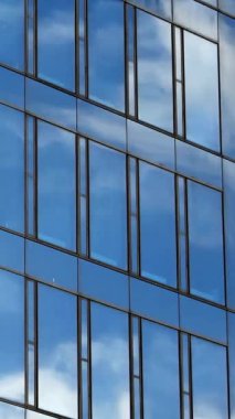 Bir ofis binasının cam cephesinden yansıyan bulutlarla dolu mavi bir gökyüzünün zaman akışı.