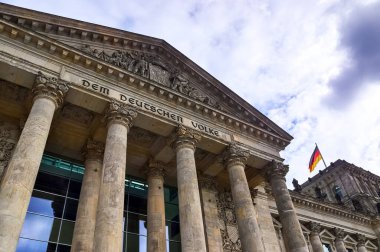 Berlin, Almanya - 03. Ekim 2024: Almanya 'nın başkenti Berlin' de Alman bayrağı dalgalanırken Reichstag binasının ön cephesinin düşük açılı görüntüsü