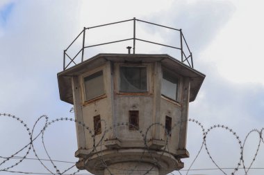 Berlin, Almanya - 03. Ekim 2024: Berlin, Almanya 'da, bulutlu gökyüzüne karşı dikenli tellerin üzerinden yükselen eski terk edilmiş muhafız kulesi