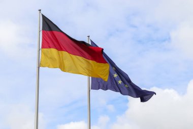 Almanya ve Avrupa Birliği bayrakları mavi gökyüzüne karşı bayrak direkleri sallıyor.