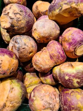 Süpermarkette üst üste yığılmış taze şalgamların yakın plan görüntüsü mor ve sarı renklerini gözler önüne seriyor.