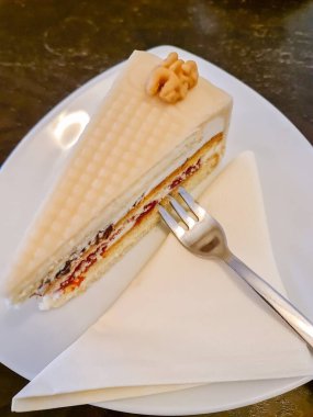 Küçük bir cevizle süslenmiş, beyaz bir tabakta çatal ve peçeteyle servis edilen badem ezmesi soslu lezzetli bir pasta dilimi.