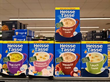 Hamburg, Almanya - 04. Şubat 2025: Tai Curry, Knoblauch, Waldpilz ve Lauch gibi çeşitli Heisse Tasse hazır çorbaları bir mağaza rafında sergilenmektedir.