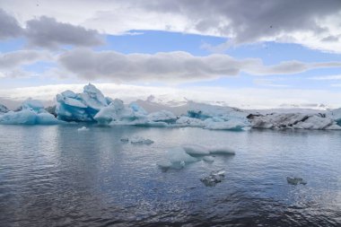 Buzdağları İzlanda 'daki Jokulsarlon buzul gölünde yüzüyor bulutlu bir gökyüzünün altında nefes kesici bir manzara yaratıyorlar.