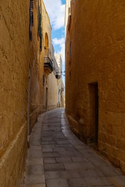 Mdina, Malta 30 Eylül 2024: Mdina 'da taş duvarlar ve mavi gökyüzü ile güneşli dar bir sokak
