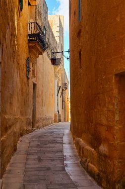 Mdina, Malta 30 Eylül 2024: Tarihi Mdina 'da taştan binalar ve balkonlarla aydınlatılmış ara sokak