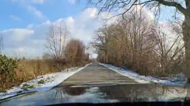 Kışın güneşli bir havada dar bir kırsal yolda hareket halindeki bir arabadan manzara.